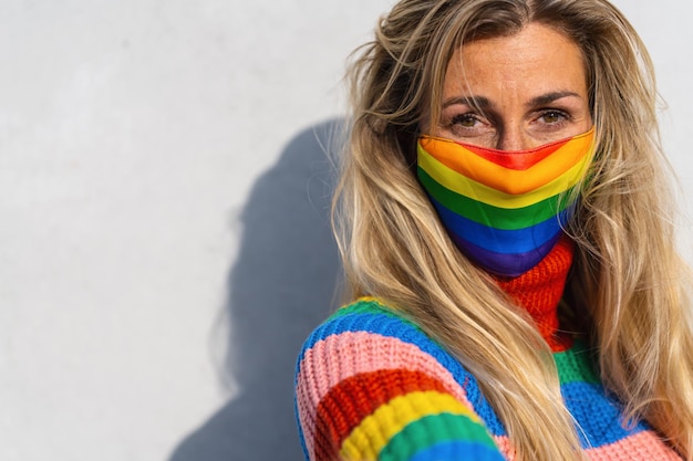 Giovane lesbica sorridente sulla fotocamera mentre indossa una maschera arcobaleno per proteggere gli altri dalla pandemia di Coronavirus Focus sul viso