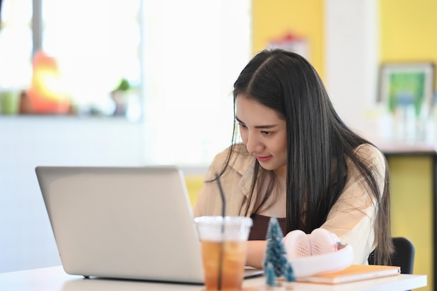 Giovane libera professionista seduta al suo posto di lavoro e concentrata lavorando sul computer portatile.