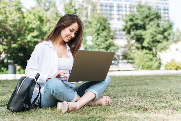 Giovane libera professionista studentessa asiatica con i capelli lunghi che lavora al computer portatile nel parco cittadino