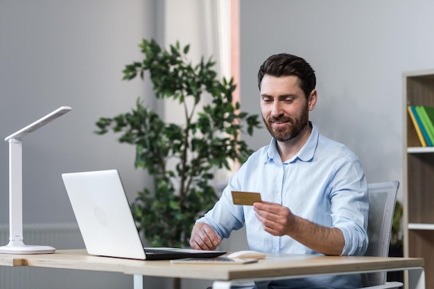 Giovane libero professionista che lavora in ufficio al computer alla scrivania Tiene una carta di credito lavora con il conto denaro effettua ordini