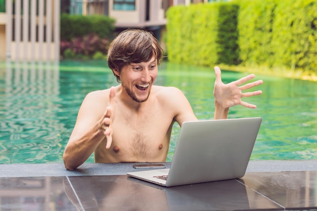 Giovane libero professionista che lavora in vacanza accanto alla piscina.