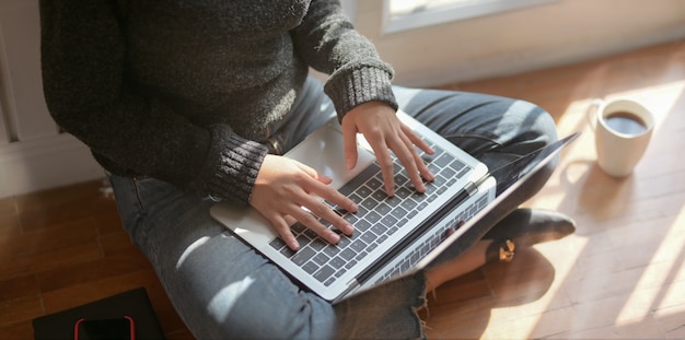 giovane libero professionista femmina digitando sul computer portatile mentre era seduto accanto alle finestre
