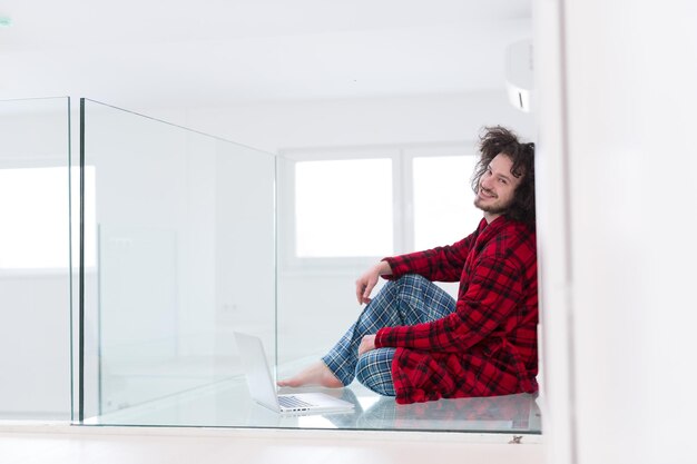 giovane libero professionista in accappatoio che lavora da casa utilizzando il computer portatile mentre è seduto sul pavimento