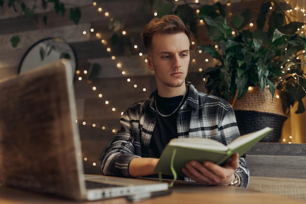 giovane libero professionista maschio che legge le note sul taccuino mentre lavora a un progetto remoto al tavolo