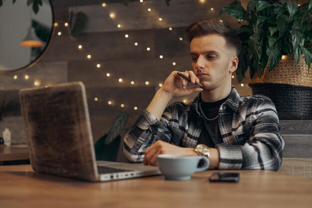 Giovane libero professionista maschio serio che utilizza il computer portatile e lavora al progetto mentre si siede al tavolo in un caffè