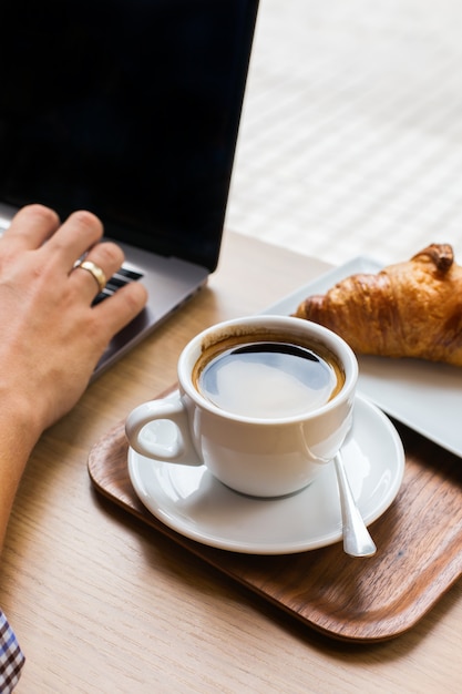 Giovane, libero professionista seduto in un bar, bevendo caffè e lavorando su un laptop. Composizione lifestyle con luce naturale