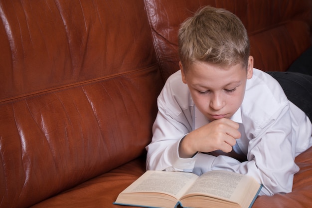 Giovane libro di lettura del ragazzo sul sofà a casa