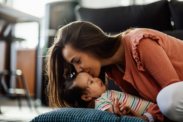 Giovane madre amorevole che bacia la sua bambina mentre trascorre del tempo insieme a casa