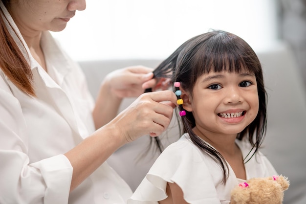 Giovane madre asiatica che lega i capelli della figlia