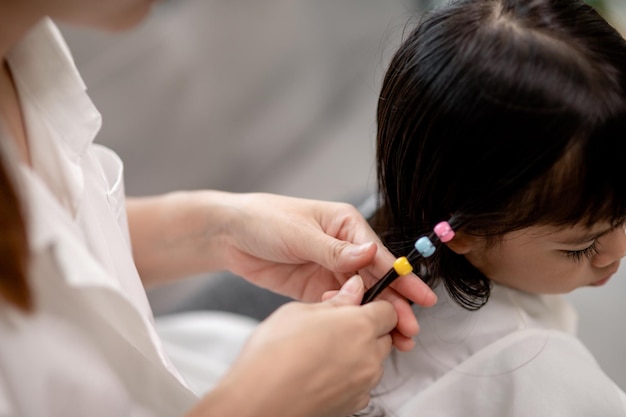 Giovane madre asiatica che lega i capelli della figlia