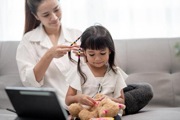 Giovane madre asiatica che lega i capelli della figlia