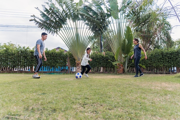 Giovane madre asiatica, padre e figlia che giocano a calcio all'aperto nella natura di un parco giardino. Bambino di famiglia felice divertente giocare a calcio insieme in estate, sport ed esercizi per uno stile di vita sano