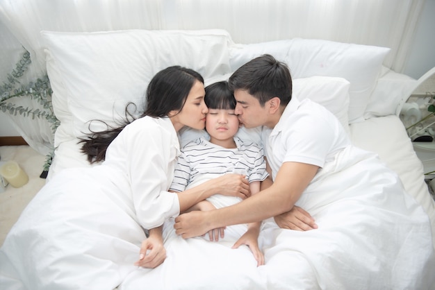 Giovane madre asiatica, padre e ragazzo che dormono nel letto, mamma e papà bacio sulla guancia del figlio, vista dall'alto