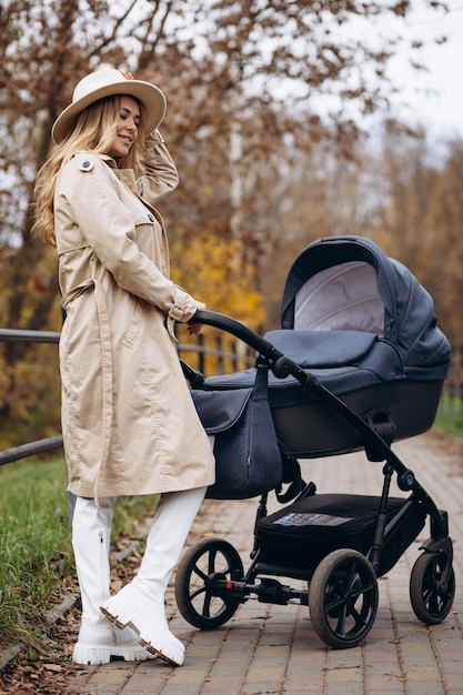 Giovane madre che cammina con il passeggino e il suo neonato nel parco