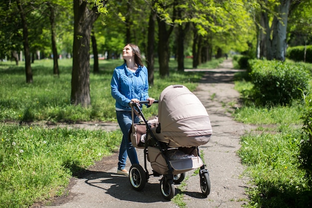 Giovane madre che cammina e spinge un passeggino nel parco