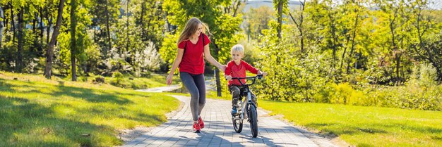 Giovane madre che insegna a suo figlio come andare in bicicletta nel formato lungo dell'insegna del parco