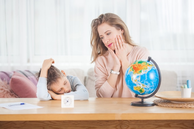 Giovane madre che insegna al suo piccolo figlio a casa. Mamma e suo figlio studiano la geografia al chiuso