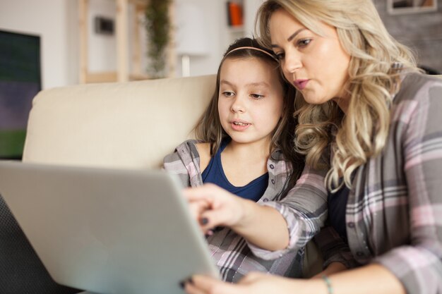 Giovane madre che punta al laptop mentre naviga su Internet con sua figlia