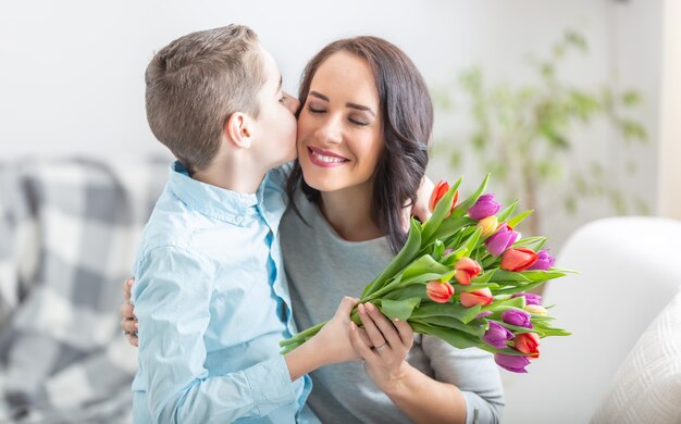 Giovane madre che riceve un bouquet pieno di tulipani e un bacio affettuoso da suo figlio durante la festa nazionale delle madri.