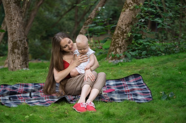 Giovane madre che tiene in braccio il suo bambino e si siede su una coperta da picnic. Maternità felice.