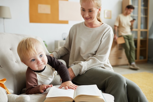 Giovane madre con bambino che gioca sul divano e legge un libro con il padre a casa