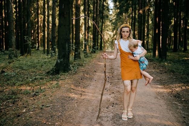 Giovane madre con il bastone che tiene suo figlio nella foresta