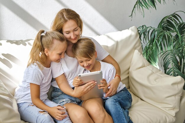 Giovane madre con la figlia e il ragazzo dei bambini che utilizzano il dispositivo del computer della compressa digitale