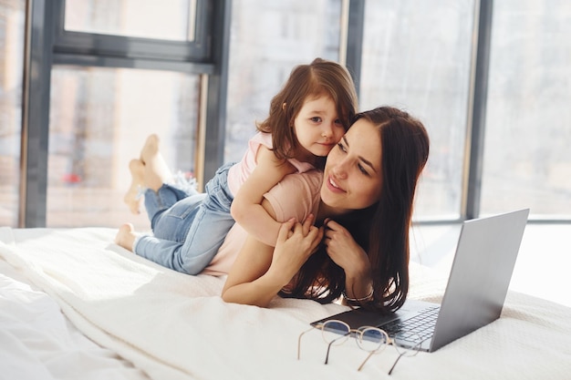 Giovane madre con sua figlia che trascorrono il fine settimana insieme in camera e usano il laptop