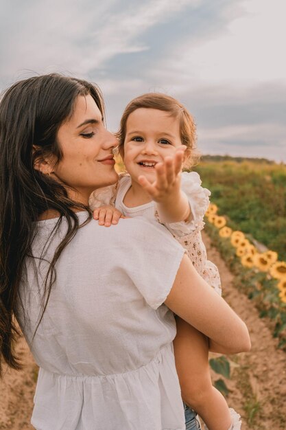 Giovane madre con sua figlia nel mezzo di un campo di girasoli al tramonto