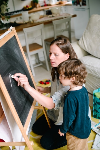 Giovane madre disegno gesso sulla lavagna con il suo giovane figlio a casa