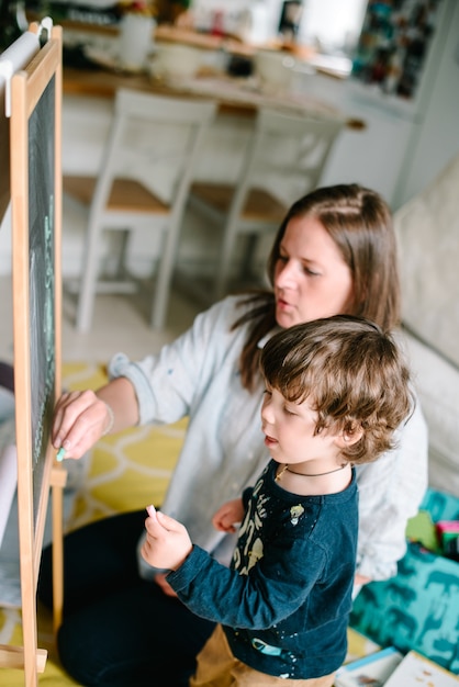 Giovane madre disegno gesso sulla lavagna con il suo giovane figlio a casa