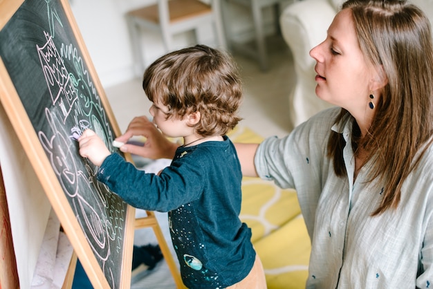 Giovane madre disegno gesso sulla lavagna con il suo giovane figlio a casa