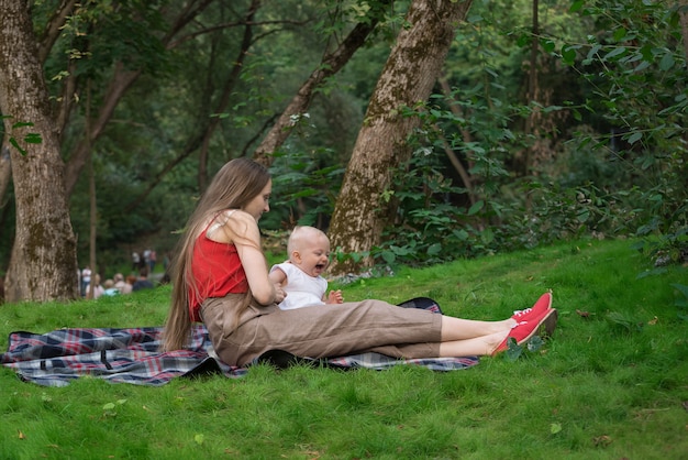 Giovane madre e bambino seduto in un parco su una coperta da picnic. Weekend con il bambino all'aperto