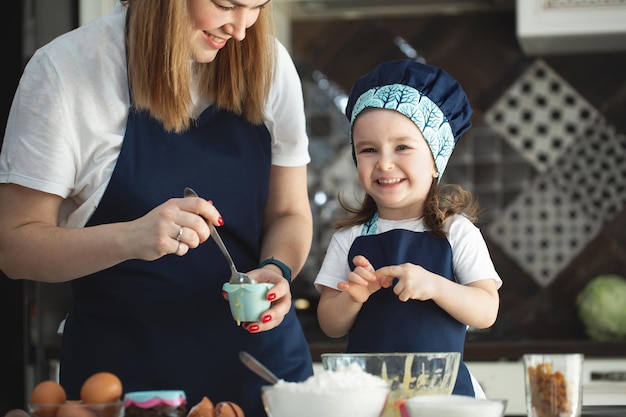Giovane madre e figlia in cucina che preparano cupcakes e sorridono ridendo