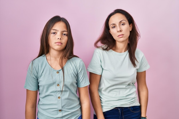 Giovane madre e figlia in piedi su sfondo rosa che sembrano assonnate e stanche, esauste per la stanchezza e i postumi di una sbornia, occhi pigri al mattino.