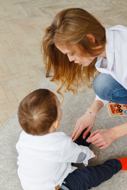 Giovane madre e figlio carino giocano insieme seduti sul pavimento nel soggiorno