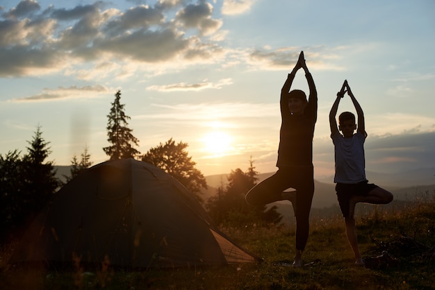 Giovane madre e figlio che fanno ginnastica alle montagne al tramonto. Madre e figlio che fanno yoga. Addestramento della donna e del bambino nella natura. Sport all'aperto. Stile di vita sportivo sano.