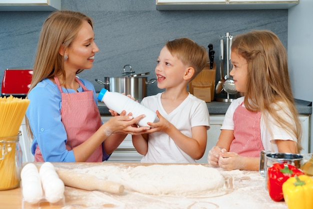 Giovane madre e i suoi bambini carini che cucinano pizza insieme in cucina