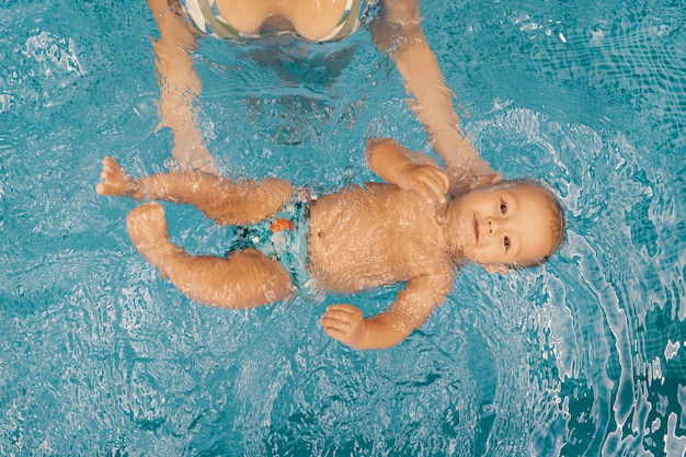 Giovane madre e il suo bambino godendo di una lezione di nuoto per bambini in piscina. Bambino che si diverte in acqua con la mamma