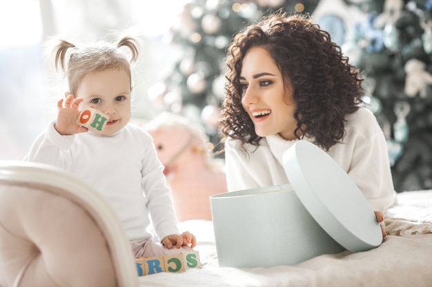 Giovane madre e sua figlia divertirsi vicino all'albero di Natale in casa