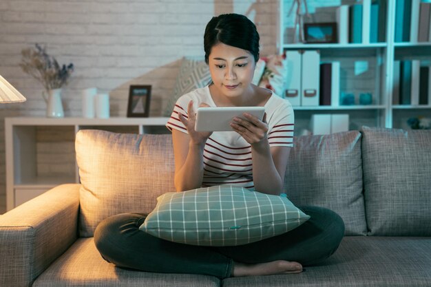 giovane madre elegante e apprendimento online del sito Web di studio dopo il sonno del bambino. casalinga duro lavoro studio su tavoletta digitale stare sveglio fino a tarda notte nel buio soggiorno a casa sorridente touch screen