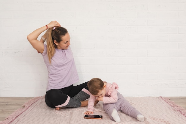 giovane madre fa esercizi sportivi a casa e sua figlia di 1 anno utilizza il concetto di maternità multifunzionale smartphone