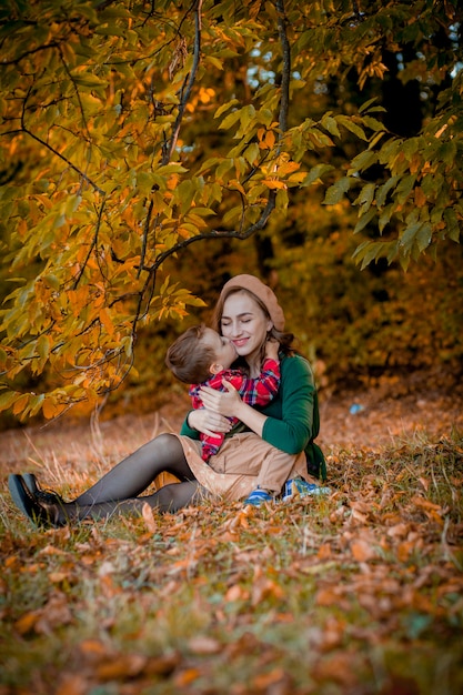 Giovane madre felice che gioca e che si diverte con il suo piccolo figlio del bambino il giorno caldo di autunno del sole nel parco.