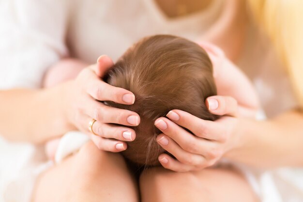 Giovane madre felice che tiene il suo bambino in camera da letto, ritratto del primo piano. Primo piano della testa del bambino nelle mani della mamma, del lave familiare e del concetto tenero