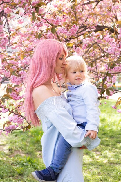 Giovane madre in abito blu che gioca con il suo bambino sorridente e godendo dell'atmosfera primaverile sullo sfondo dei lillà in fiore Felice maternità Felice infanzia Momenti inestimabili in famiglia