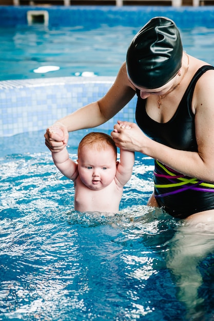 Giovane madre, istruttore di nuoto e bambina felice in piscina per bambini. Insegna al neonato a nuotare. Goditi il primo giorno di nuoto in acqua. La mamma tiene la mano bambino che si prepara per le immersioni. facendo esercizi