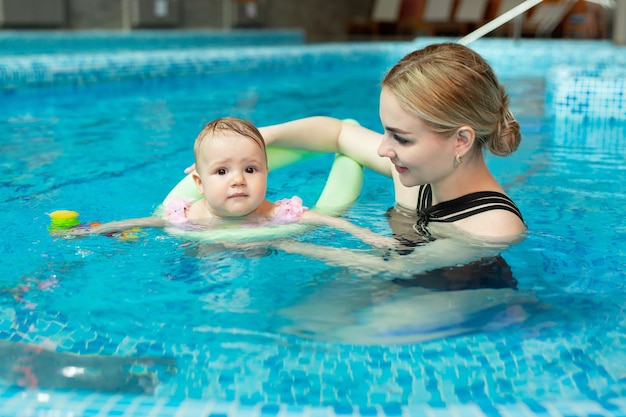 Giovane madre istruttrice di nuoto e bambina felice in piscina Insegna al bambino a nuotare