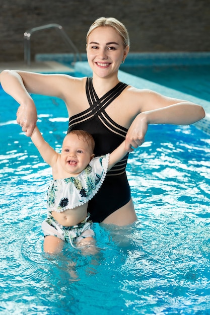 Giovane madre, istruttrice di nuoto e bambina felice in piscina. Insegna al neonato a nuotare.