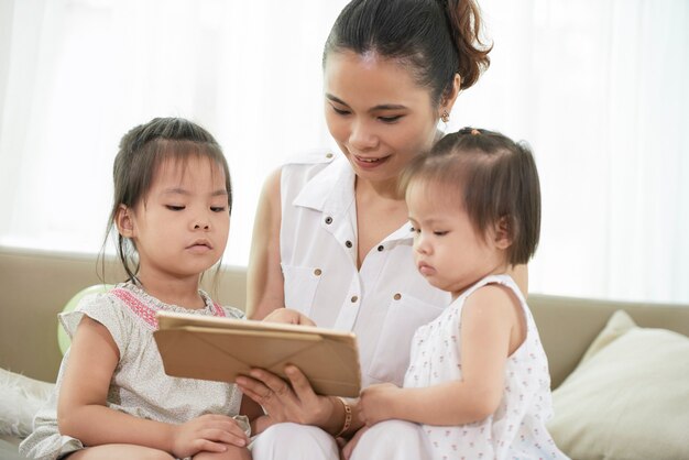 Giovane madre positiva che spiega alla piccola figlia come giocare sul tablet digitale