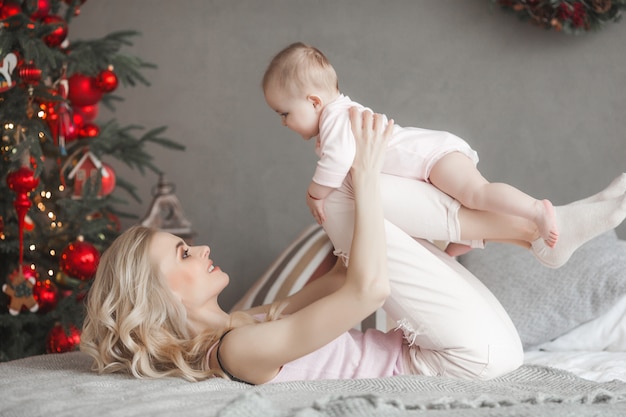 Giovane madre prendersi cura della sua piccola bambina. Bella mamma e sua figlia in casa in camera da letto. Famiglia amorevole. Mamma attraente che tiene il suo bambino.